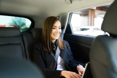 Mutlu bir iş kadını, bir taksiye binerken dizüstü bilgisayarı üzerinde çalışırken gülümsüyor. Bir arabanın arkasında bilgisayarda daktilo yazmakla meşgul bir iş kadını.