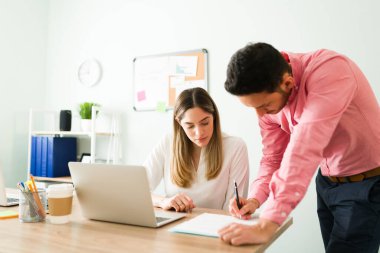 Yakışıklı patron, bayan bir iş arkadaşının masasının yanında dururken kontrat imzalıyor. İş ortakları çalışıyor ve iş belgelerini kontrol ediyor.