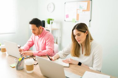 Çekici iş arkadaşları masalarında oturup ofiste birlikte çalışırlar. Beyaz kadın ve Latin adam toplantı odasında yazı yazıyorlar.