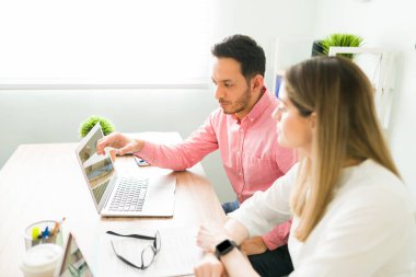 İspanyol erkek patron dizüstü bilgisayardaki analitik rapora bakıyor ve kadın iş arkadaşına ve profesyonel meslektaşına iş sunumunu anlatıyor. 