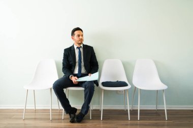 Takım elbiseli yakışıklı İspanyol bir adam işe alım ofisinde özgeçmişiyle oturmuş iş görüşmesi için randevu bekliyor. 