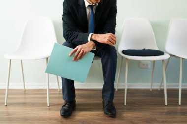 Profesyonel bir adam resepsiyonda oturuyor ve iş görüşmesini beklerken elinde özgeçmişi olan bir dosya tutuyor. İş adamı, işe alım bürosunda randevu bekliyor.