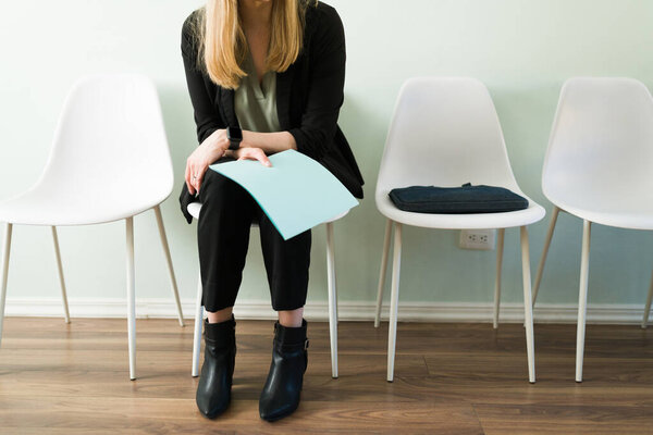 Professional caucasian woman sitting at reception and holding a folder with her resume while waiting for a job interview. Business woman waiting for an appointment in a recruitment office