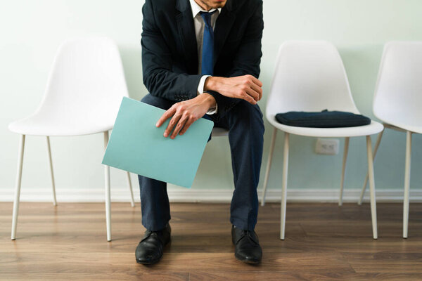 Professional man sitting at reception and holding a folder with a resume while waiting for a job interview. Businessman waiting for an appointment in a recruitment office