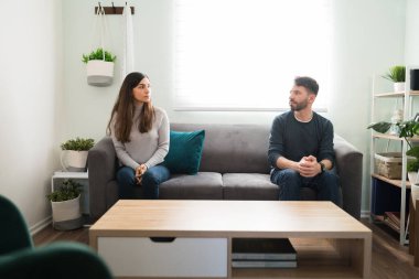 İlişkilerindeki sorunlar yüzünden kavga ettikten sonra oturma odasındaki kanepede otururken birbirlerine öfkeyle bakan genç çift.