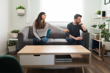 Üzgün eş, sorunlarını konuştuktan sonra yakışıklı kocasıyla barışmaya çalışıyor. Genç bir kadın evdeki kanepede otururken erkek arkadaşından af diliyor.