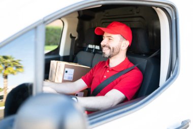 30 'lu yaşlarda, şehirde çalışan ve teslimat kamyonu kullanan mutlu bir adamın yan görüntüsü. İspanyol kurye gün içinde paket teslim ediyor.