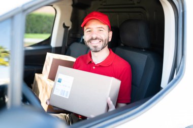 Mutlu erkek kurye teslimat kamyonuyla teslimat adresine geliyor ve elinde küçük bir paket var. Teslimatçı gülümseyerek müşteriyi karşılamaya hazırlanıyor.