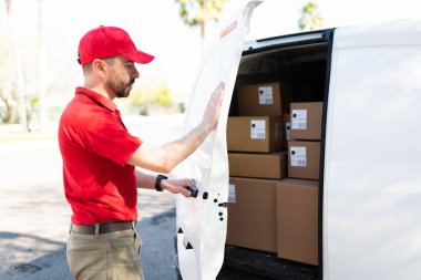 Erkek İspanyol kurye mesaisi bittikten sonra beyaz bir minibüsün arka kapısını kapatıyor. Paketleri teslim etmek için kamyonet kullanan çekici bir işçi.