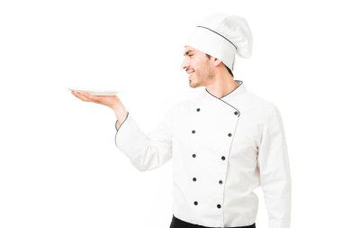 Üniformalı çekici bir aşçının profili öğle yemeğinde tabak servis ederken ya da beyaz arka planda yemek yerken. Profesyonel şef bir restoranda boş tabak tutuyor. 