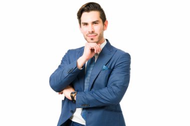 Beyaz bir arkaplanda poz veren yakışıklı profesyonel bir avukat. Düşünceli bir iş adamı çenesindeki elle göz teması kuruyor. 