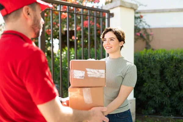 Attractive young woman holding some packages from a male courier. Caucasian woman receiving some parcels from a delivery man at her doorstep