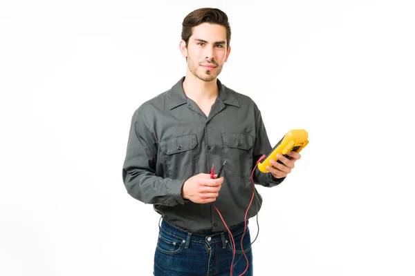 一个严肃的年轻人拿着一个万用表当电工 西班牙男性技师进行眼神交流并使用工作工具 — 图库照片