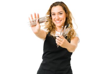 Makyajcı elinde fırçayla kuaförde eğleniyor. Önlük takan ve güzellik tasarımcısı olarak çalışan neşeli genç bir kadın. 