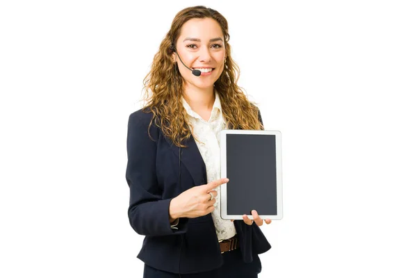 一个带着耳机笑着指着平板电脑屏幕的快乐美丽女人的画像 担任推销员的年轻职业女性 — 图库照片
