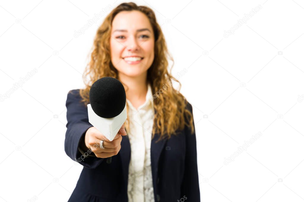 Happy journalist holding up a microphone while doing a live interview for the tv news. Female reporter interviewing someone against a white background