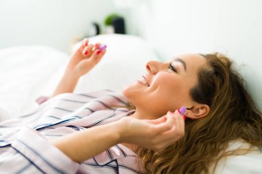 Gürültüden kaçmak için pijamalı, kulak tıkacı takan genç bir kadının yan görüntüsü.