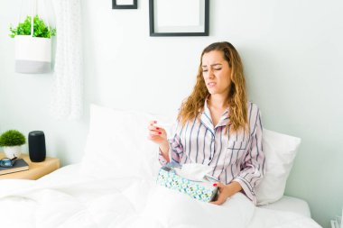 Ateşi ve gribi olan hasta İspanyol kadın sabah yatağında dinlenirken ateşini kontrol ediyor. 