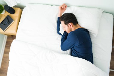 Pijamalı Latin bir adam sıcak bir yatakta uyur ve yorganla kaplıdır. Yorgun bir adam yatak odasında hayal kurup dinleniyor.