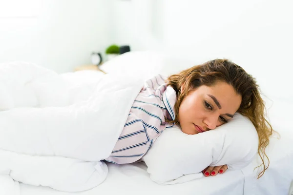 悲しいラテン語の女性は彼女の胃の上に横たわって気分が悪く落ち込んでいる 可愛いです女性嘘でベッドに覆われていますホワイトDuvet — ストック写真