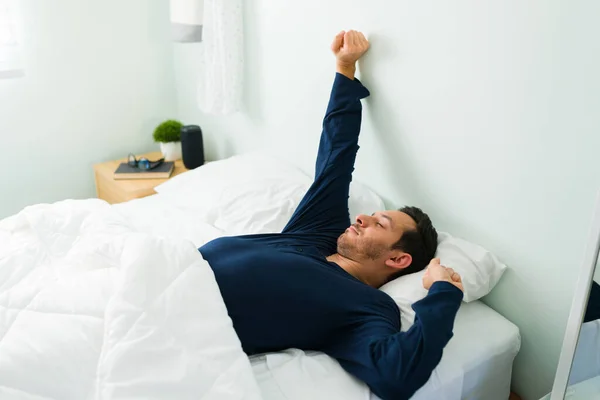 醒来时 一个穿着睡衣躺在床上的有魅力的男人伸出手来 西班牙人躺在舒适的床上 感觉很好 — 图库照片