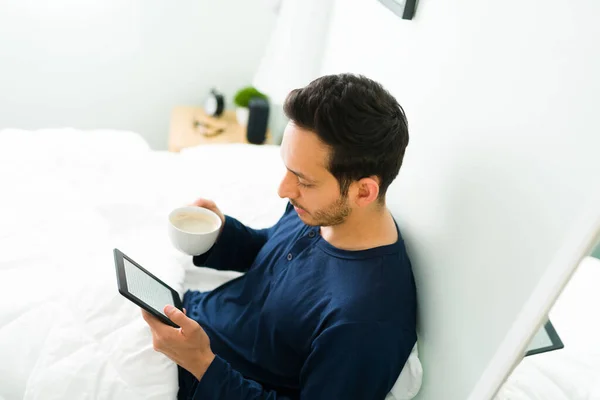 三十多岁的英俊男子穿着睡衣躺在床上 用电子阅读器或平板电脑看书 — 图库照片