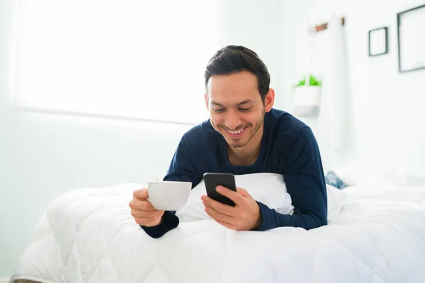 Homem Hispânico Feliz Pjs Mensagens Texto Seu Smartphone Enquanto Descansa — Fotografia de Stock