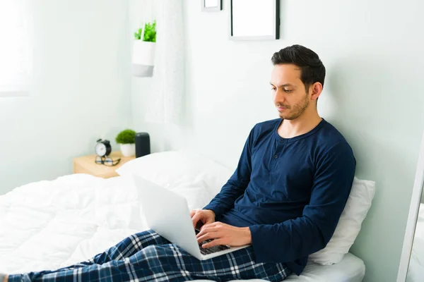 Hombre Atractivo Escribiendo Ordenador Portátil Trabajando Mientras Está Sentado Cama —  Fotos de Stock