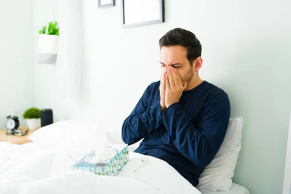 パジャマを着たラテン系の病気の男は ベッドで休んでいる間にインフルエンザのために組織で鼻を吹いて — ストック写真