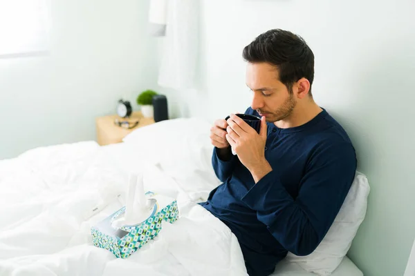 一个患流感的年轻人早晨躺在舒适的床上 感觉很糟糕 喝了一杯热茶 感觉很好 — 图库照片