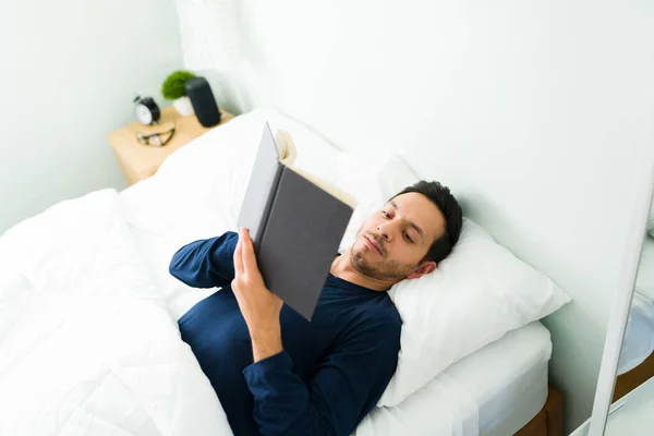 一个拉丁年轻人躺在床上 在卧室里看书 迷人的30多岁的男人享受着周末的早晨 — 图库照片