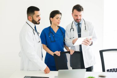 Doktorlar ve hemşire bir hastanın durumunu tartışıyor ve bir tablette bilgi gösteriyorlar. Sağlık kurulu toplantı odasında birlikte çalışıyor.