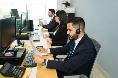 Kulaklık okuma talimatları olan ve elinde evrak tutan Latin bir adamın yan görüntüsü. Tele-pazarlama ve müşteri hizmetlerinde çalışan satış temsilcisi 
