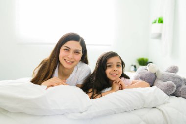 Ailecek vakit geçiriyoruz. Uyandıktan sonra yatak odasında dinlenirken gülümseyen mutlu bir anne ve küçük kızın portresi. 