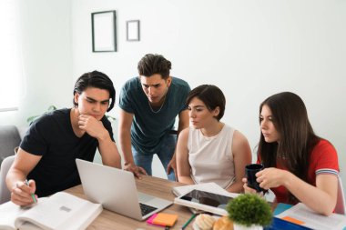 Akıllı genç kadınlar ve erkekler evde birlikte ödev yaparken dizüstü bilgisayarlarında bir üniversite metni okumaya odaklanıyorlar.