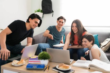 Çeşitli üniversiteli arkadaşlar ders çalışmaya ara verip gülerken dizüstü bilgisayardan komik bir video izliyorlar.