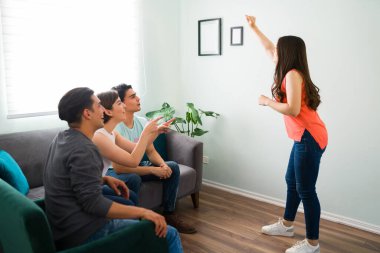 Oturma odasında sessiz sinema oynarken arkadaşlarına bir kelime anlatmaya çalışan beyaz bir kadın.