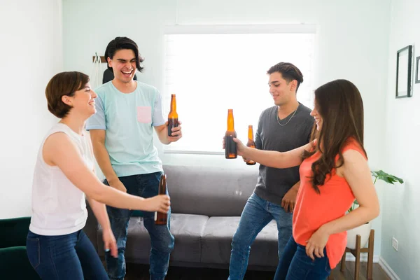 It\'s time to party! Cheerful college friends drinking beer and laughing while dancing an upbeat song in the living room