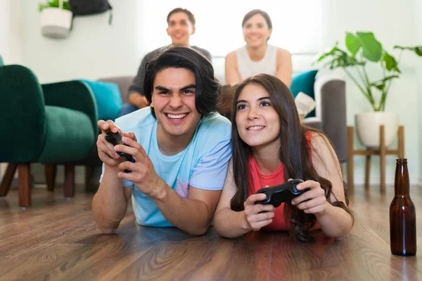 这对迷人的夫妇躺在客厅地板上 专心致志地和朋友一起在电视上玩电子游戏 — 图库照片