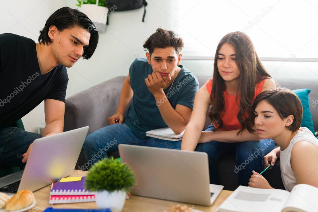 Smart young woman showing her laptop screen and explaining to her college friends how to do the homework