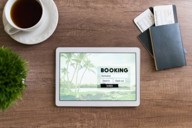 Bir seyahat acentesindeki ahşap bir masanın en üst görüntüsü. Tablet, rezervasyon bilgileri, pasaportlar ve bir fincan sıcak kahvenin yanındaki uçak biletleri.