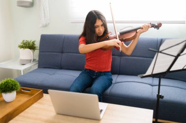 Bilgisayarındaki bir video görüşmesi sırasında müzik öğretmeninin talimatlarına uyan ve evde keman çalmayı öğrenen güzel bir kız.