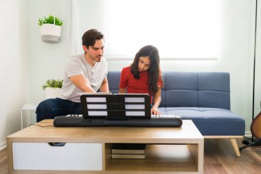 Yakışıklı piyano öğretmeni öğrencisine talimat veriyor. Evde resim dersleri sırasında müzik notalarıyla klavye çalma pratiği yapan küçük bir kız.
