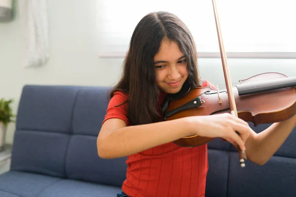 バイオリンを弾いている子供 ラテン系の女の子が笑顔で家で音楽のレッスンを練習しています 新しい楽器を演奏することを学ぶためにオンラインクラスを取る若い学生 — ストック写真