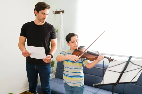 スペイン語の教師が子供の音楽スキルをレビューします 芸術的な少年は楽譜を読み プライベートレッスン中にバイオリンを弾いています — ストック写真
