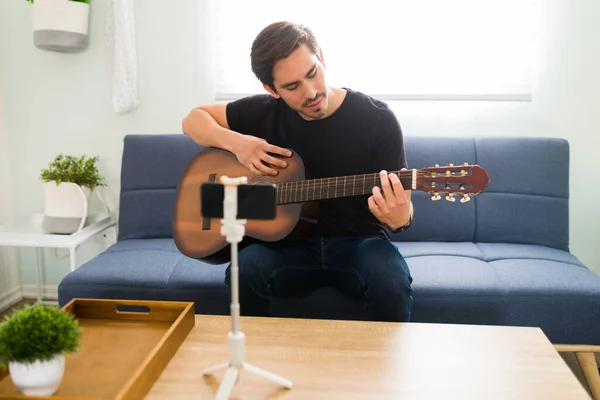 アコースティックギターで歌を演奏しながらスマートフォンでオンライン音楽レッスンを行う才能豊かな芸術家 — ストック写真