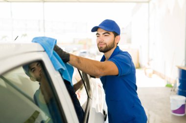 Oto yıkamada temizledikten sonra aracın suyunu kurutan tatmin olmuş erkek işçi. Oto yıkama servisinde çalışan genç adam. 