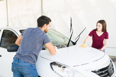 Çekici erkek arkadaş ve kız arkadaş oto yıkamada arabalarını yıkıyorlar. Kaputu ve ön camı temizleyen çift.