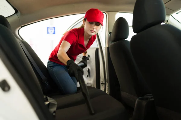 Finishing the job at the auto detailing service. Caucasian young woman using a vacuum cleaner on the dirty car seats at the car wash