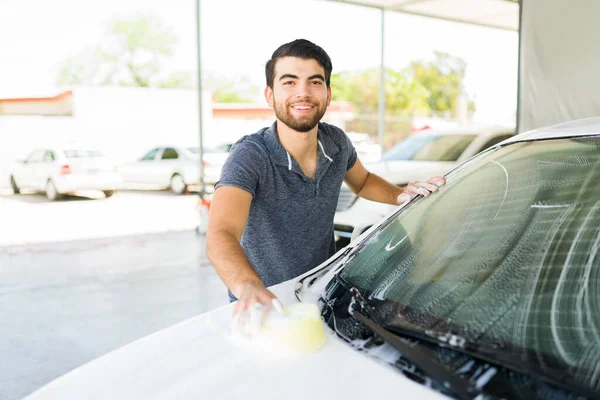 I prefer to wash my own car. Portrait of a handsome young man smiling and making eye contact while washing the windshield at a self service car wash